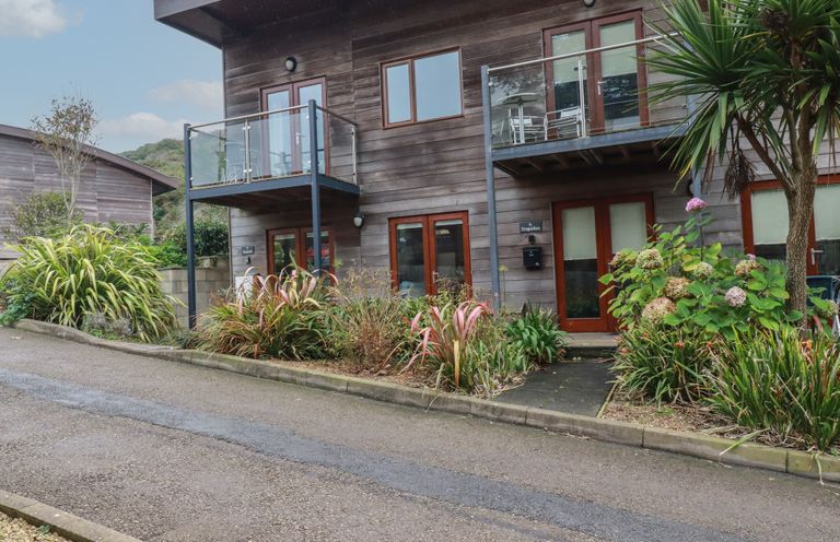 A wooden two-story building with glass balconies and plants in front at Tregullan in Porthtowan