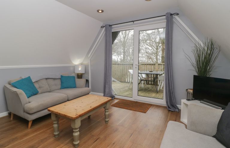 A living room with a wooden coffee table two sofas and a television near glass doors leading to a balcony at Valley Lodge 38 in St Ann's Chapel Cornwall