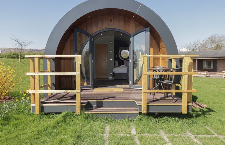 A pod with an arched roof and glass doors opening to a wooden deck with chairs and a table at The Rowan Pod in Cowbridge