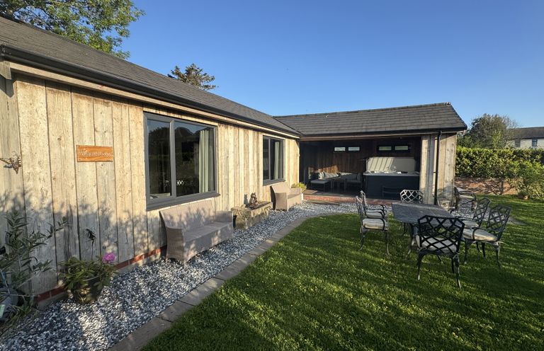 An outdoor wooden lodge with patio chairs a table a bench and a hot tub at Wayside Lodge in Blackpool