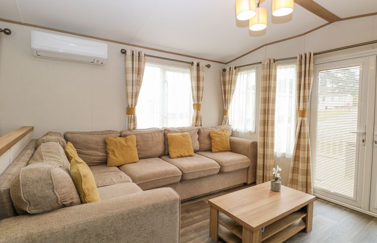 A living room with a beige sectional sofa and yellow cushions with a wooden coffee table and windows with plaid curtains at 75 Foxburrow Hang in Fritton