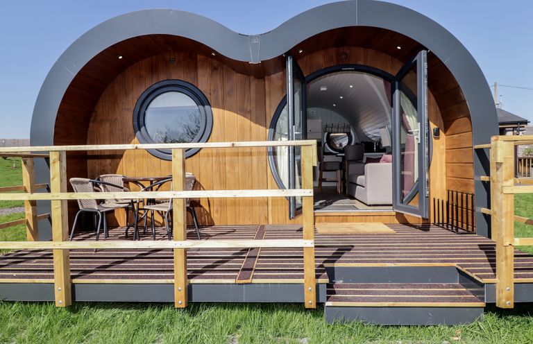 A wooden pod with curved roof and circular windows with a deck and outdoor seating at The Hazel Pod in Cowbridge