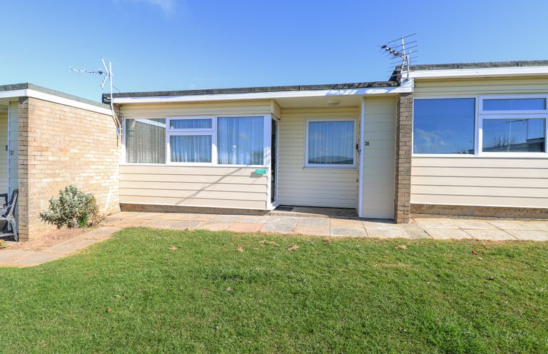 Exterior view of a single-story house with windows a door paved walkway and grass at Chalet 38 in Hemsby