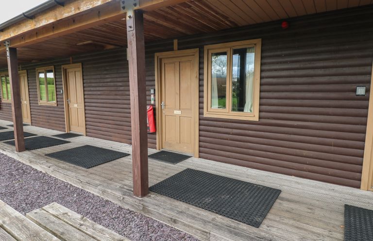 Exterior of a wooden building with brown doors and windows and a covered porch with black mats at Beech in Cowbridge