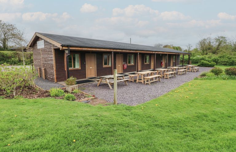 A wooden cabin with multiple doors and windows surrounded by picnic tables and green grass at Cherry in Cowbridge