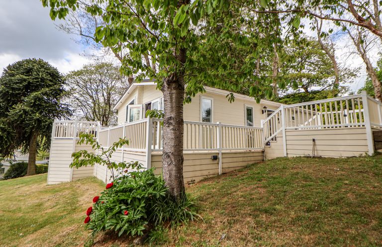 A house with a white fence and open windows on a grassy slope with trees and flowers at 155 Woodland Hall Lyons in Ruthin