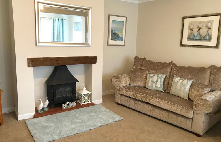 A living room with a sofa a fireplace with a mirror above it and framed pictures on the walls at Pen Y Frith Bungalow in Prestatyn