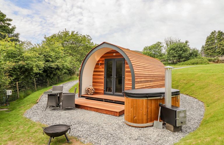 A wooden pod with glass doors next to a hot tub and outdoor furniture at Briallen in Bontddu near Dolgellau