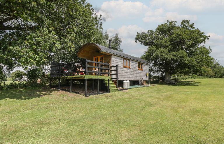 A hut with a deck surrounded by grass and trees at Shepherd Hut’s in Bristol