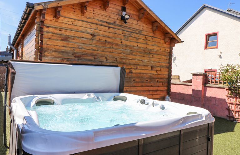 An outdoor hot tub with bubbling water next to a wooden cabin and a fenced yard at Smiddy Bothy in Edzell