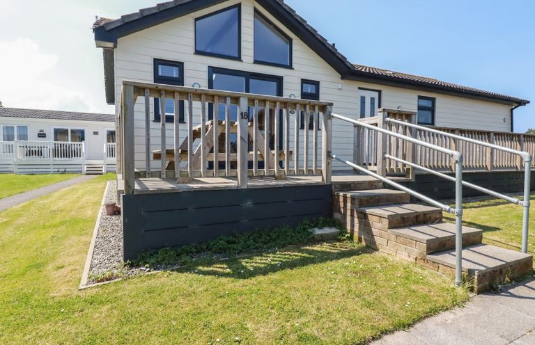 A single-story house with wooden railings and steps leading to the entrance at Lodge 18 in St Merryn