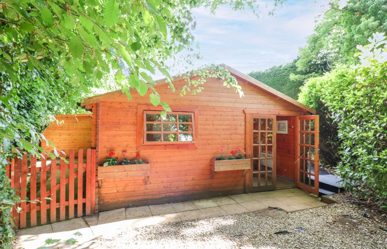 A wooden building with a door and window in an outdoor area at Stumps Cross Lodge Upper Coscombe near Winchcombe