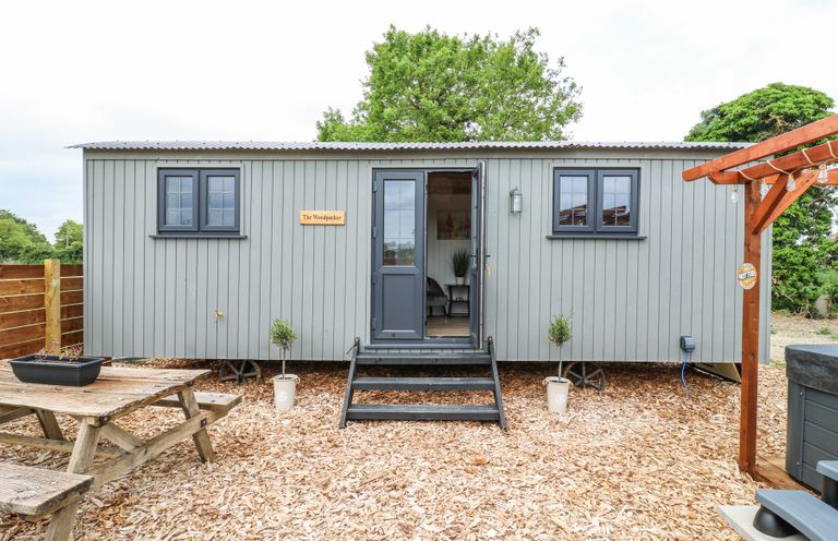 A small grey cabin with a picnic table and hot tub outside at Woodpecker in Lode near Bottisham