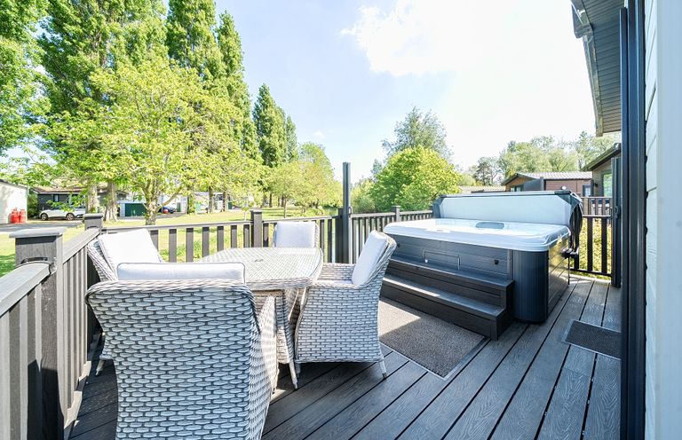An outdoor deck with a table and four chairs and a hot tub at Lakeside Lullaby Billing Aquadrome Holiday Park