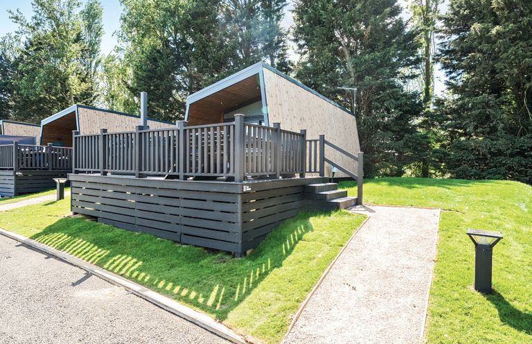Wooden cabins with fenced decks on grassy area surrounded by trees at Moonlit Skylight - Billing Aquadrome in Billing Aquadrome Holiday Park