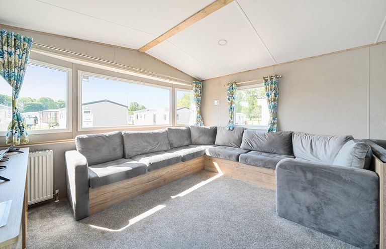A lounge area with a large grey L shaped sofa and windows with floral curtains at Brookside Bliss Billing Aquadrome