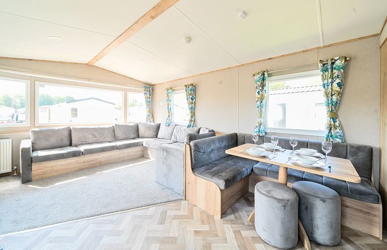 A living area with a grey sectional sofa and a dining table set with plates and glasses at Sunset Sands - Hayling Island in Hayling Island Holiday Park