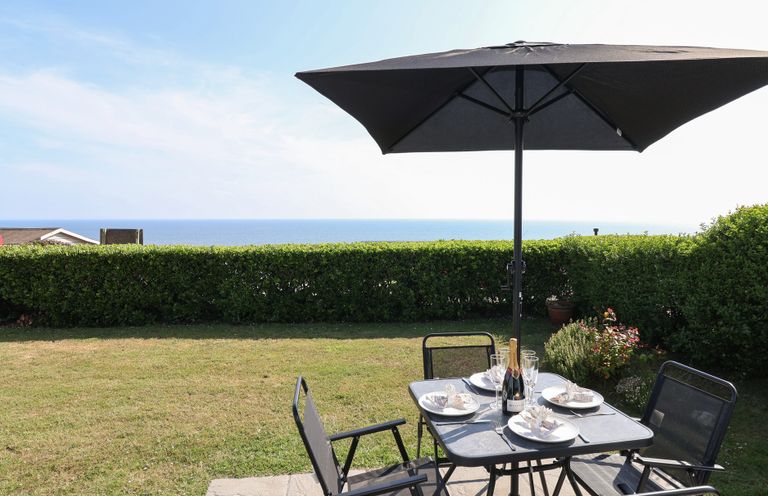 A garden with a table, chairs, and umbrella overlooking the sea at Stella Maris in Torpoint