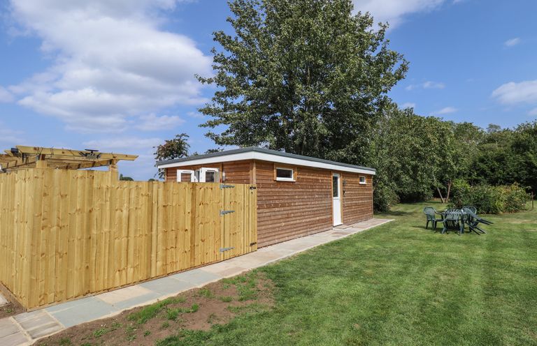 A shed with a fence and seating in a garden at Pear Tree Lodge in Alford