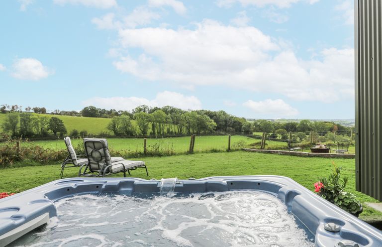 A hot tub with outdoor chairs and a green landscape at Brondel Luxury Shepherd's Hut in