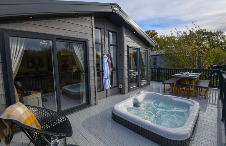 An outdoor terrace with a hot tub and dining table at Lakewood Retreat Woodhall Spa