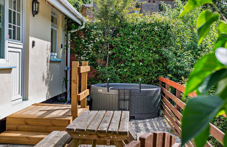 A garden with a hot tub and wooden furniture at Kernow Nook Spa, Perranporth