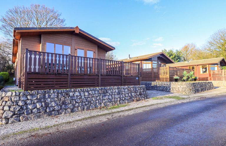 A log cabin with a deck and stone wall at Kingfisher Lodge