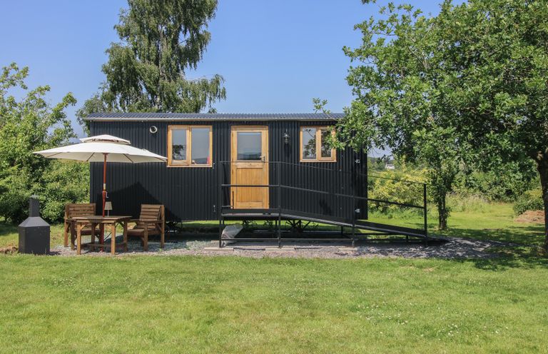 A black shed with windows and a ramp along with a table and chairs at Dave's Place in Broadstone near Munslow