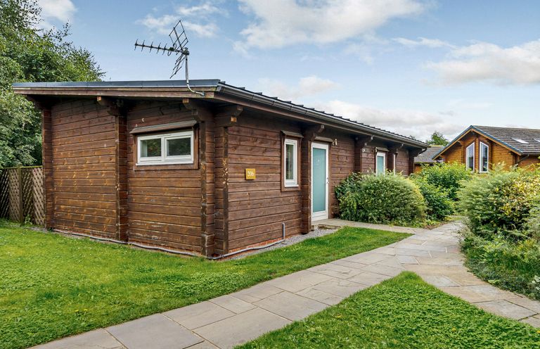 A wooden cabin with a pathway and bushes at Chestnut Spa (Pet) Carlton Miniott near Thirsk