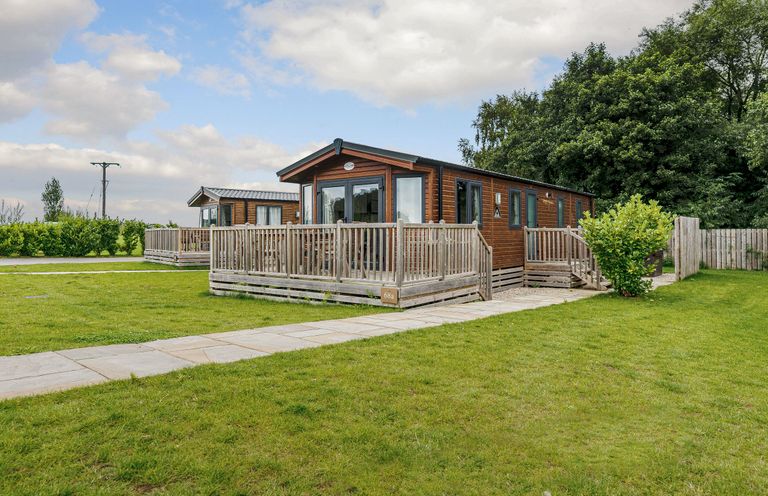 A lodge with a deck and surroundings at Alder Waterside Spa Carlton Miniott near Thirsk