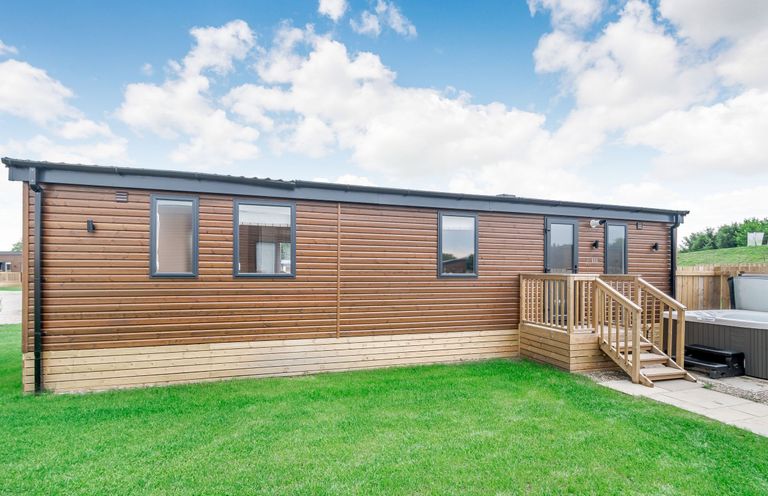 A wooden cabin exterior with grass and steps at Cedar Spa in Carlton Miniott near Thirsk