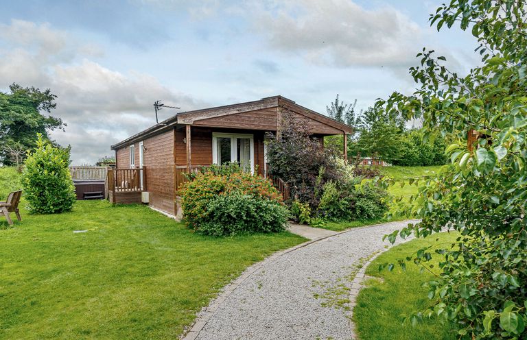 A cabin surrounded by grass and bushes at Fir Tree Waterside Spa Carlton Miniott near Thirsk