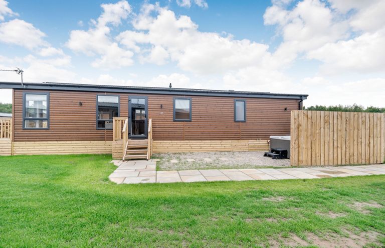An outdoor view of a mobile home with steps and a fence at Beech Waterside Spa Carlton Miniott near Thirsk