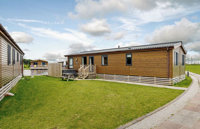 An outdoor area with a log cabin and picnic table at Larch Waterside Spa (Pet) Carlton Miniott near Thirsk