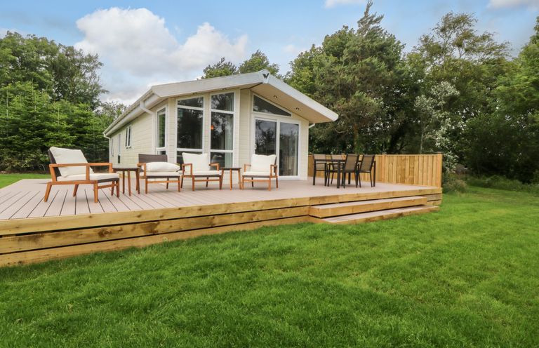 A house with a deck and chairs in a garden at Plas Marchog Lodge Rhoscefnhir near Pentraeth
