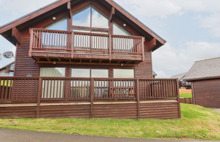 A wooden lodge with a balcony and decked area at 65 Benasa Lodge at Winnard's Perch near St Columb Major