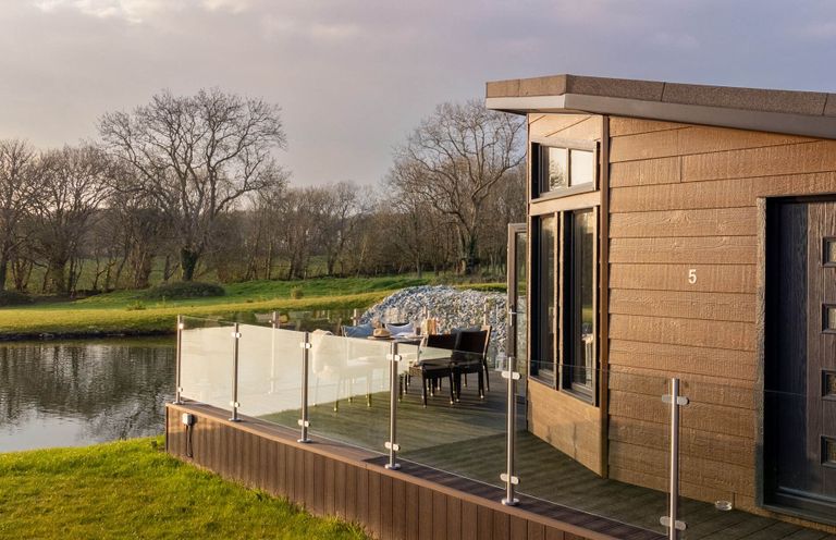 An outdoor deck with a table and chairs beside a lake at Lake View Spa in Praze-An-Beeble