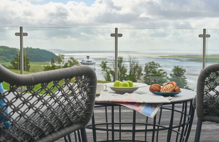 An outdoor area with a table and chairs overlooking a river at Milk Wood 3 Spa in Laugharne