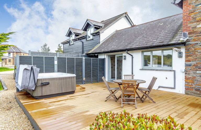 An outdoor area with a hot tub and a wooden table with chairs at 4C2 Summerleaze Garden Cottage 2 Spa Bude