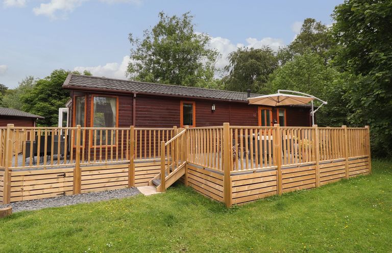 A cabin with a wooden deck and parasol at Kingfisher Lodge in Windermere