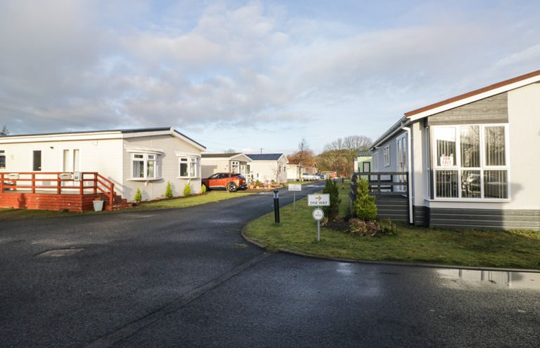 A view of mobile homes with a pathway and vehicles at Beechtree Timber Lodge 69B in Denny