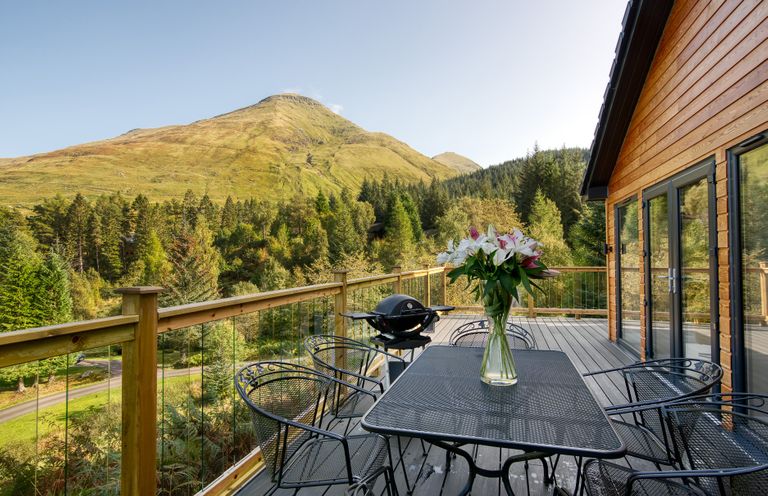 An outdoor space with a table and chairs overlooking a forest and mountain at Pinemarten Lodge Crianlarich