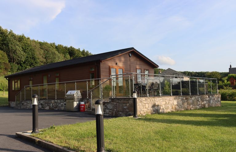 An outdoor view of a lodge with a deck and barbecue at Holly Lodge in Lloc near Caerwys
