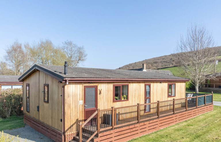 A wooden lodge with a deck and steps at Hazel Lodge in Craven Arms