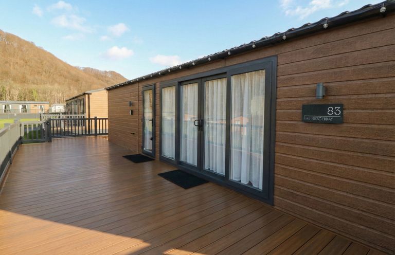 A wooden deck with sliding doors and curtains at The Ridgeway in New Quay