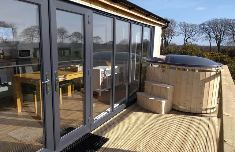 A deck with a hot tub and outdoor seating at Cleeves Cabins 2, Arran Luxury Lodge with hot tub in St. John's Town Of Dalry
