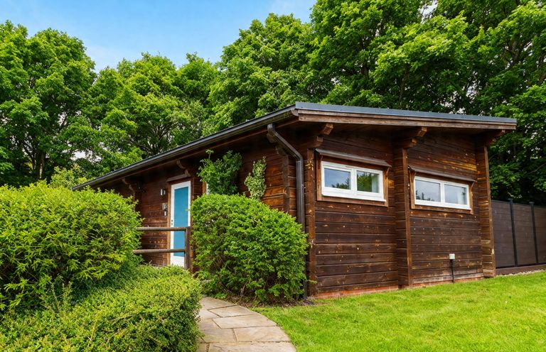 A wooden house with a blue door and bushes at Pine Lodge Spa Carlton Miniott near Thirsk