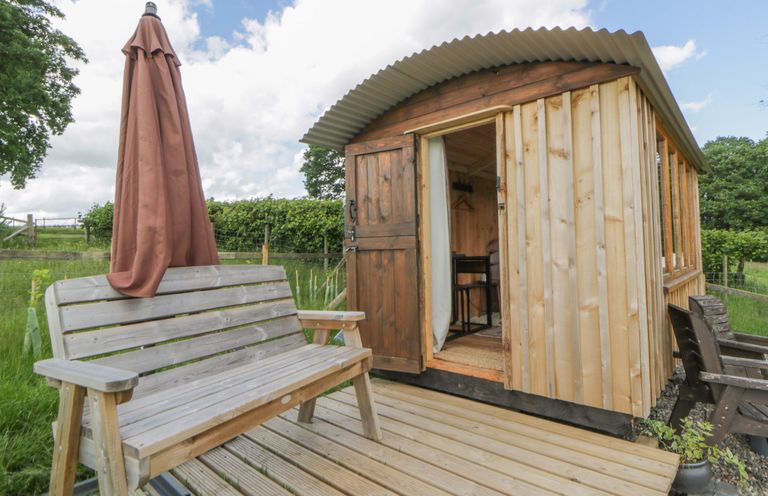 A hut with a wooden deck and umbrella at The Little Shepherds Hut with a View Builth Wells