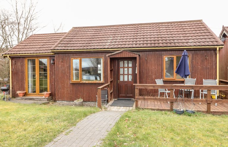A wooden house with a tiled roof a paved path leading to the front door and outdoor seating on a deck with an umbrella at Glen Dessary in Corpach near Fort William