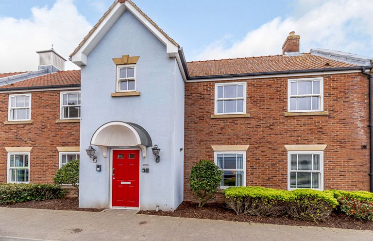 Front of a building with blue and brick walls red door and windows with shrubs at Sunrise The Bay near Filey